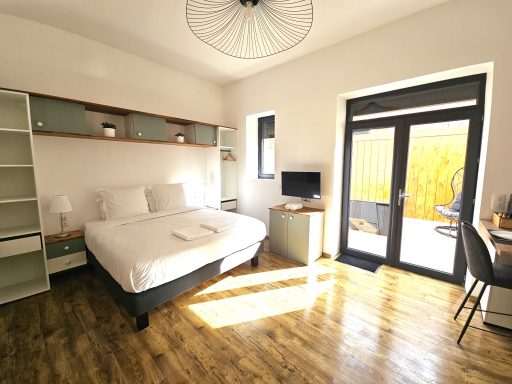 Chambre lumineuse avec un lit double, bureau, télévision et accès à un patio.
