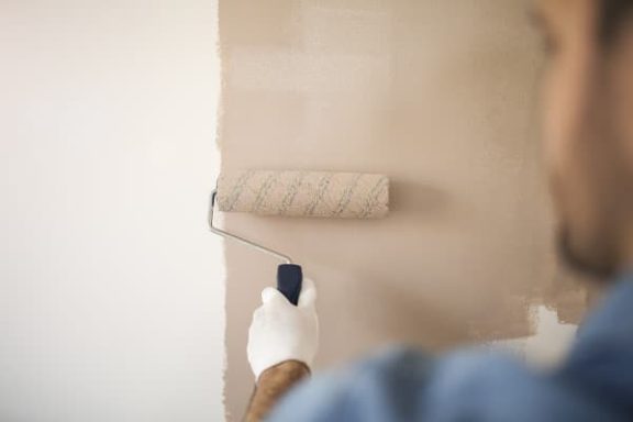 Person appliquant de la peinture beige sur un mur avec un rouleau.