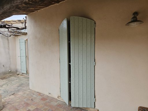 Porte à double battant en bois vert clair, ouverte sur un mur en crépi.