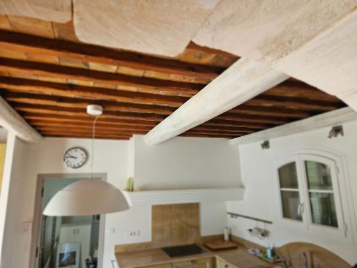 Cuisine lumineuse avec poutres apparentes, horloge, et meuble clair.