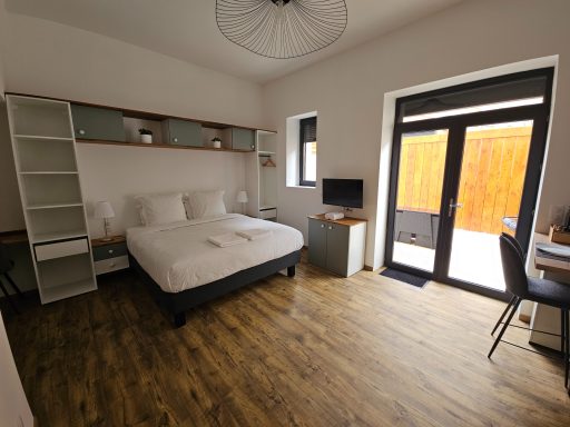 Chambre lumineuse avec lit double, bureau, télévision et accès à un patio.