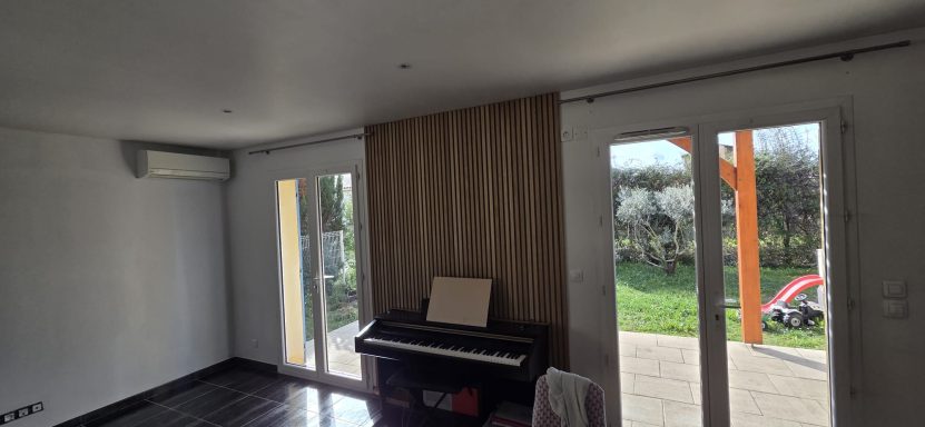Intérieur d'une pièce avec un piano, fenêtre et rideaux, vue sur un jardin.